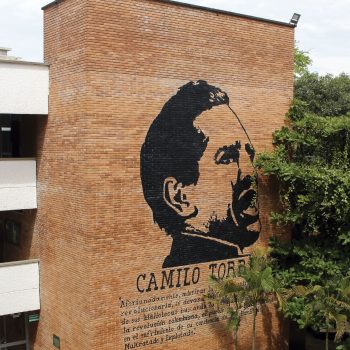 Foto tomada en la Facultad de Ciencias UIS en un plano general donde se puede apreciar una de las paredes del edificio de la facultad la cual tiene un mural de Camilo Torres junto con una leyenda.